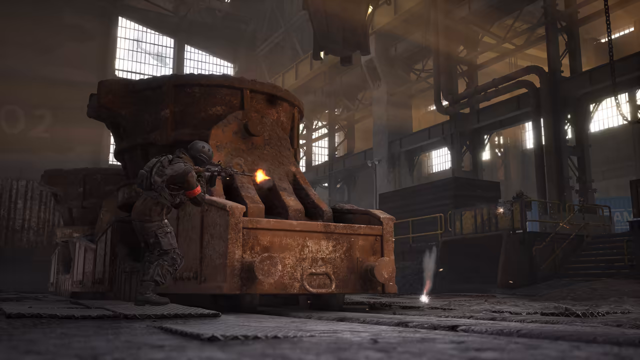 Inside a large factory hall with tall windows, pipes and gantries, a soldier crouches against a huge rusted casting ladle and fires a rifle, a muzzle flash at its end; sparks fly on the floor.