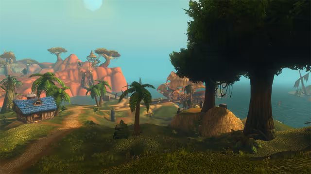 A worn dirt path leads past a small half-timbered cottage with a blue tiled roof and palm trees toward wooden docks where a large sailing ship lies moored. Big leafy trees stand on the right by the water, a wrecked mast juts from the sea, and red rock hills with flat-topped trees and a thatched lookout rise on the left under a pale sun.