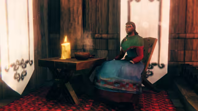 A Viking in a green shawl and blue skirt sits on a dark carved wooden chair next to a sturdy trestle table holding a lit candle and a steaming bowl, on a red carpet between two white banners.
