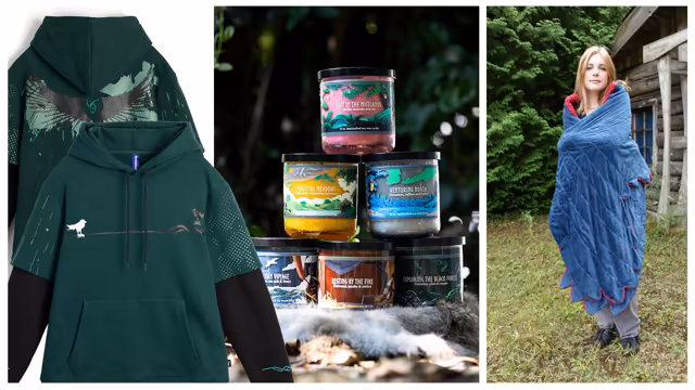 Three photographs side by side: the back and front of a dark green hoodie with black undersleeves, printed with ravens and a spread-winged emblem; a pyramid of six candle jars on a fur outdoors, labeled Lost in the Mistlands, Peaceful Meadows, Venturing North, Resting by the Fire and Exploring the Black Forest, the sixth showing a ship; and a young woman wrapped in a blue quilted blanket with red-edged, feather-shaped hems, standing on grass beside a log cabin.