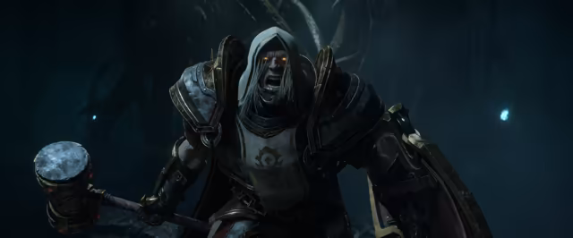 In a dark cavern hung with roots and small blue lights, a gray-faced, long-haired undead figure in a hood and heavy dark plate armor shouts toward the viewer with glowing orange eyes. A white tabard bearing the Horde emblem covers the chest, and the figure holds a heavy hammer low in one hand with a large shield on the other arm.