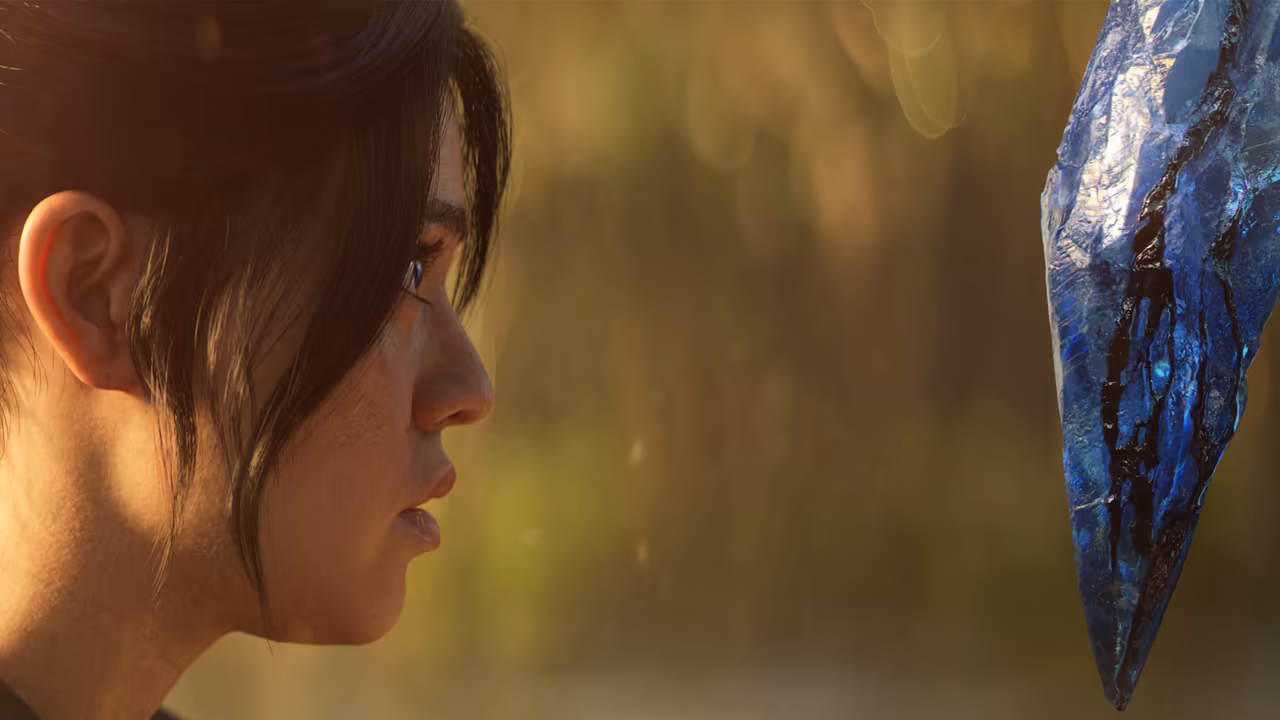 Close profile of a young woman's face on the left, dark hair falling over her ear, eyes on a long jagged blue crystal with black streaks that hangs in the right of the frame against a blurred golden background.