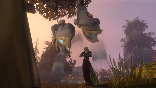 Seen from low among tall grass, a figure with long pale teal hair, pointed ears and glowing eyes stands in a long dark robe with arms folded. Above and behind, huge gray stone plates edged in gold, one set with a glowing blue gem, hover over misty, translucent limbs, framed by trees with dark foliage, a building with a blue tiled roof and a violet sky.