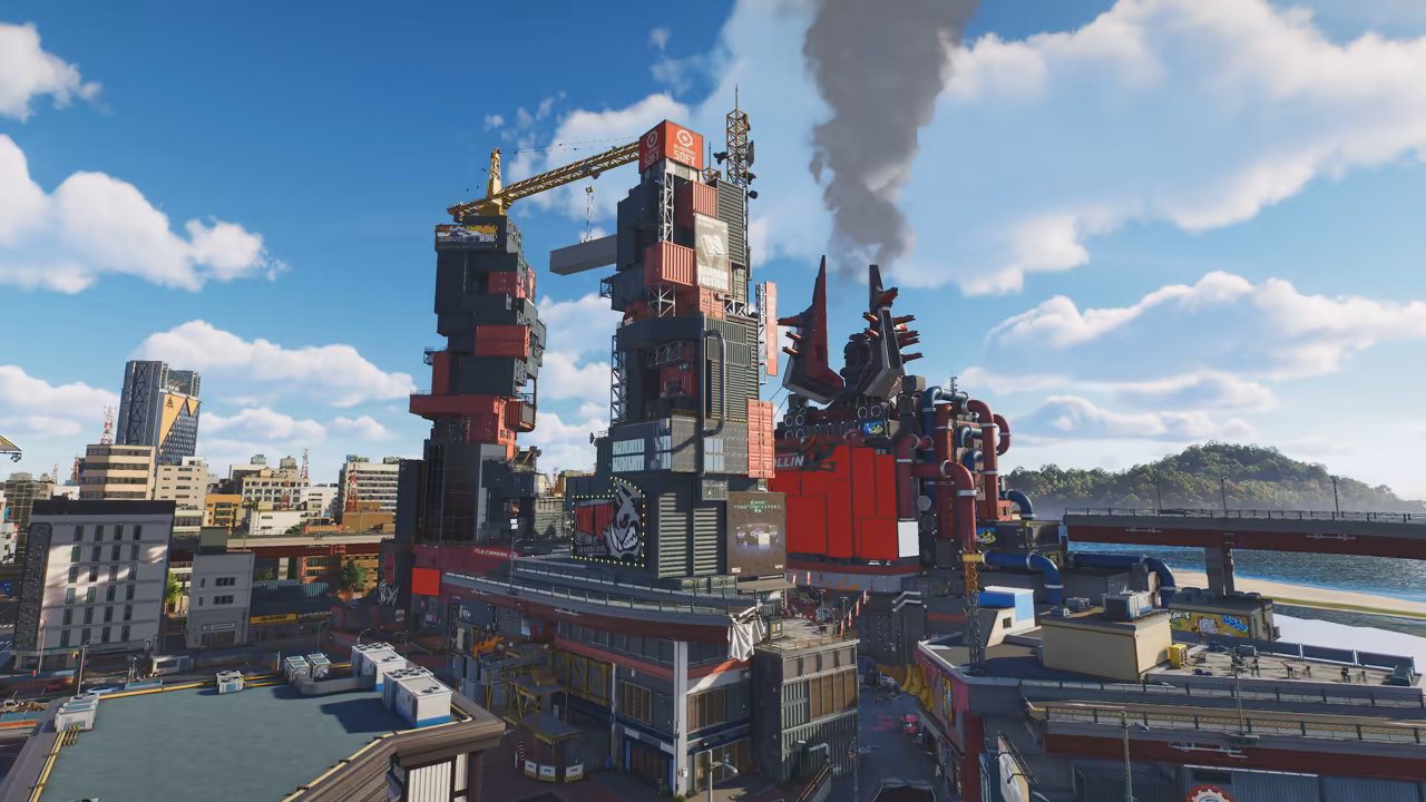 A sunny waterfront: a tall tower of stacked shipping containers with billboards and a yellow crane on top, and beside it a red building covered in pipes and dark spikes, with gray smoke rising into a blue sky. Office blocks and towers stand at left, an elevated road runs along a beach toward a wooded hill at right, and no game interface is shown.