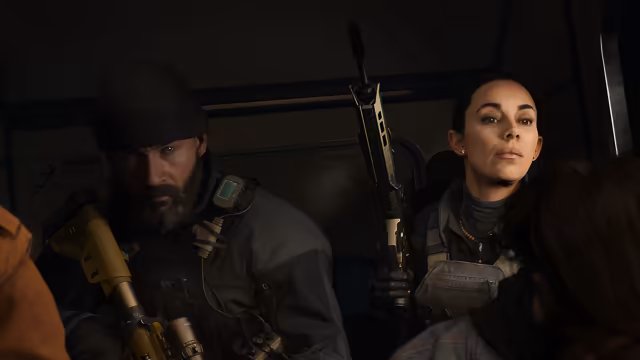 Inside a dim vehicle, a bearded man in a knit cap and tactical gear holds a rifle with a tan grip upright, beside a woman with dark hair pulled back who looks across at someone at the right edge.