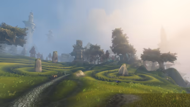 Green hills are shaped into curving terraces edged with low hedges that spiral around tall standing stones, and a cobbled path runs past a small cart toward a teal and stone tower among trees and blue-roofed houses. Tall pale towers loom through bright mist in the distance, and a purple bird walks on the grass.
