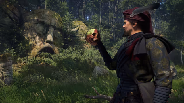 A bearded man in a dark red turban hat with a gray feather and a black brocade coat holds a skull at arm's length; behind him moss-covered rocks carved into giant faces among ferns and trees.