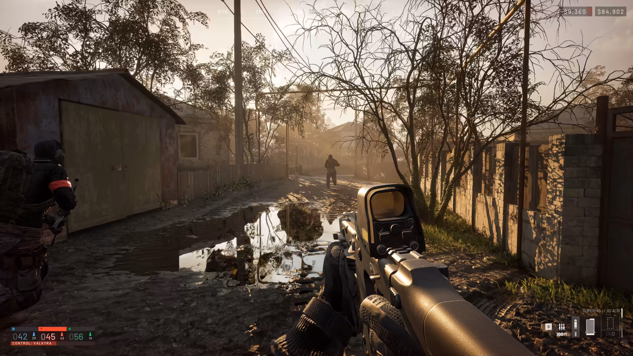 First-person view down a narrow, puddled dirt lane between garages and fences under bare trees; a teammate stands at left and a distant figure walks at the far end.