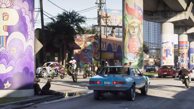 A sunny street beneath an elevated highway whose concrete pillars are painted with colorful murals; young people on dirt bikes and quad bikes ride on one wheel, a light blue sedan on large chrome wheels drives past, and two people sit against a pillar.
