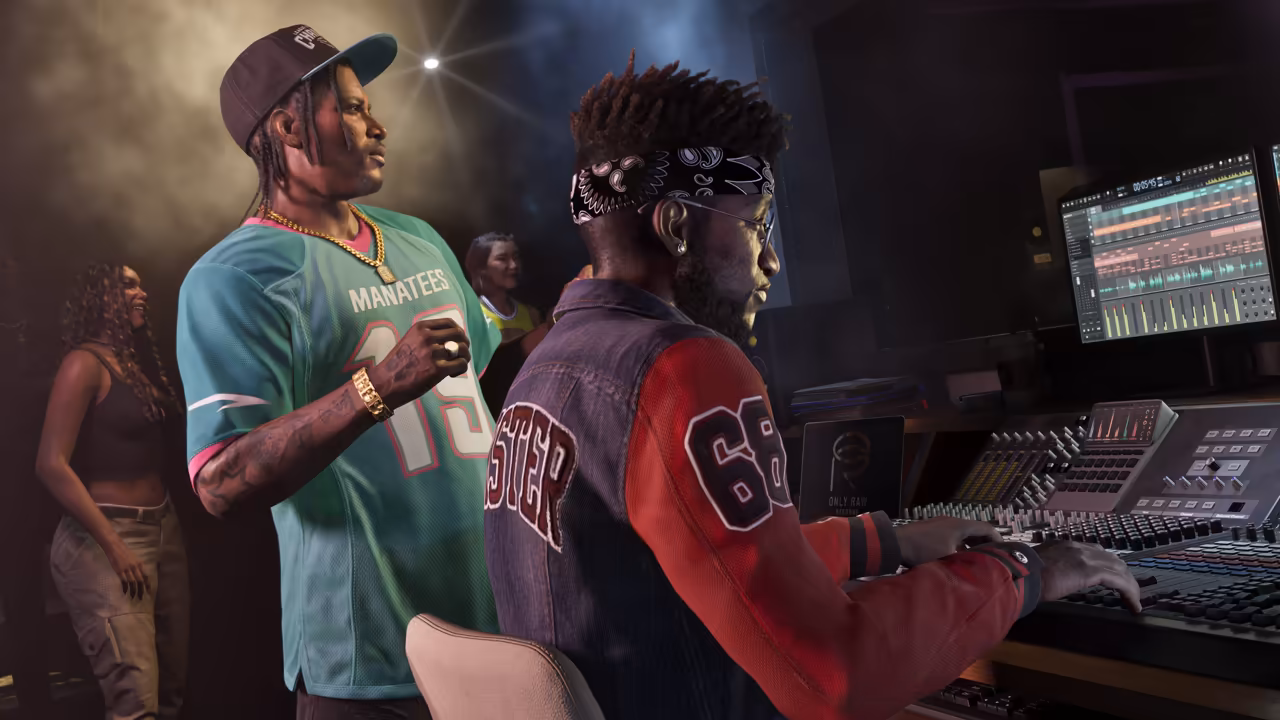 In a dim recording studio, a man with braids, a cap, gold chains and a teal Manatees football jersey watches a producer in a bandana and a varsity jacket work a large mixing console with waveforms on the screen, as two women stand in the background.