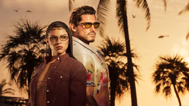 A woman with long braids, glasses and a brown denim shirt stands in front of a man with slicked hair, yellow-tinted sunglasses and a white shirt printed with flamingos and flowers, against silhouetted palm trees and an orange evening sky.