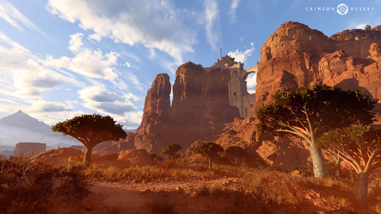 A dry canyon of tall red sandstone pillars glows in low sunlight. Flat-topped, umbrella-shaped trees grow from the scrub in the foreground, and a pale stone fortress with towers and an arched bridge clings to the cliffs above. A snowy peak rises at far left under a sky of streaky clouds.