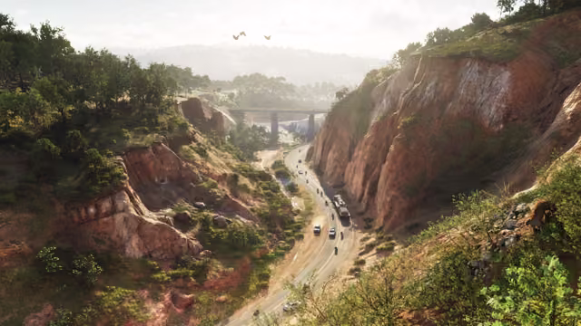 Looking down into a steep canyon with orange rock walls and dense green trees, where a road with cars and a truck runs toward a bridge in the hazy distance.