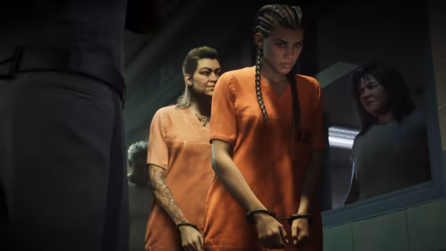 A young woman with long braids in an orange prison uniform, her hands cuffed in front of her, looks down as she waits beside an older inmate, with a guard's dark uniform in the foreground and another woman watching through a window.