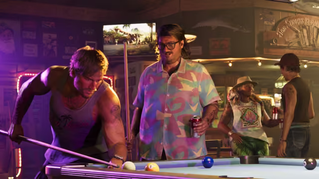 In a bar full of neon signs and memorabilia, a man in a tank top leans over a pool table to take a shot while a bearded man in glasses and a pastel patterned shirt holds a beer can and watches, and two more people chat nearby.