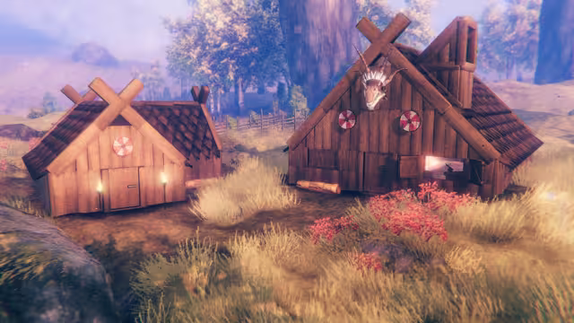 Two small wooden Viking houses with dark shingle roofs, crossed boards on the gables, round shields and a carved dragon head, standing in golden grass.