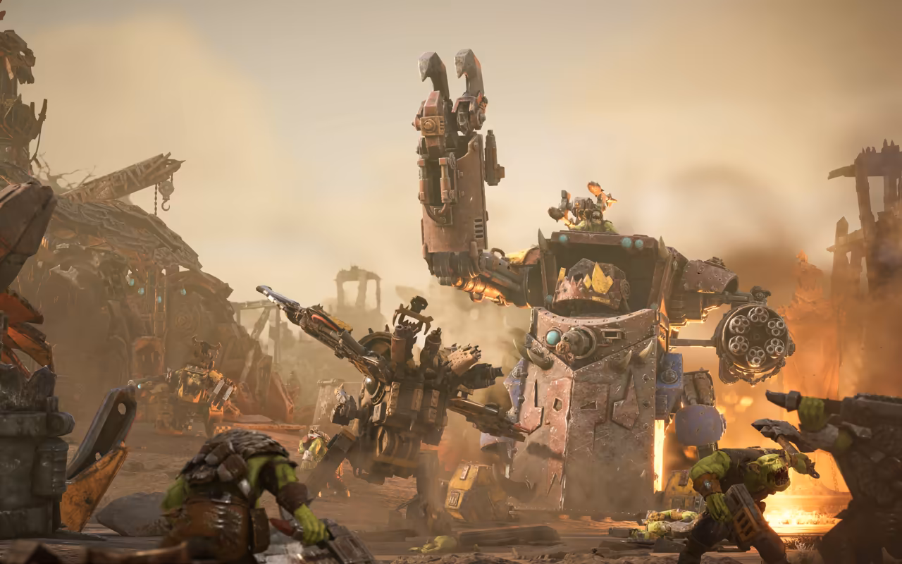 A tall boxy walker with a giant claw and a smaller walker in a tan, smoky junkyard, with Orks firing in the foreground.