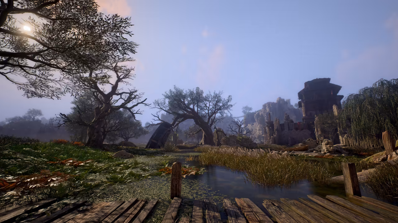 Soft early light in a hazy wetland. Weathered planks of a boardwalk fill the foreground with two posts sticking up, and green water with reeds and floating weed spreads beyond. Twisted, leaning trees stand on the banks at left and center, a crumbling square tower and broken walls stand at right beside a willow, and a pale rocky cliff rises in the mist behind. No game interface is shown.