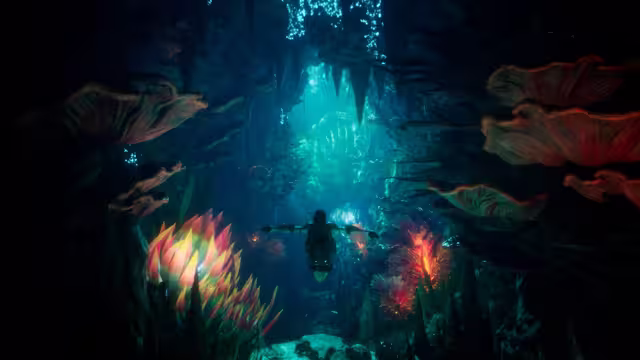 A figure swims away from the viewer through a dark blue underwater cave, framed by large pink and orange coral fans and spiky glowing anemones, toward light filtering down through the water ahead.