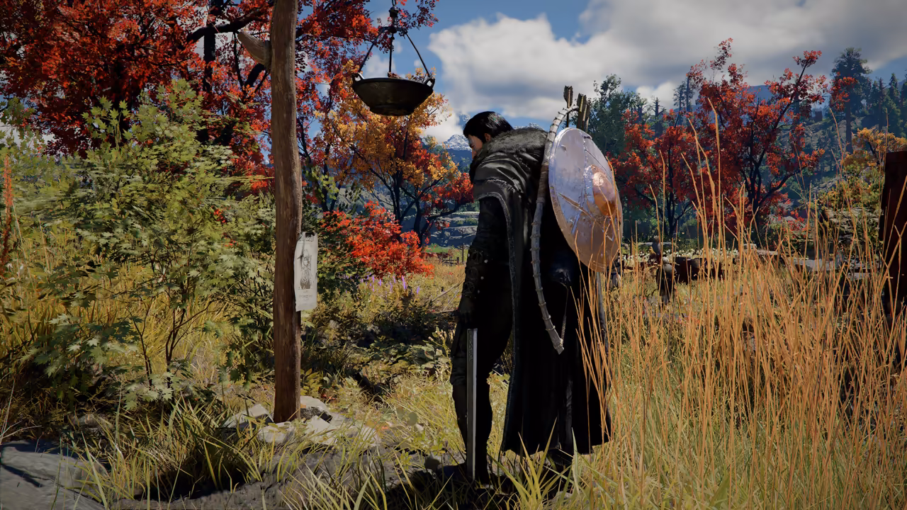 In tall golden grass among trees with red and orange leaves, a man in a dark coat with a round metal shield on his back and a sword in hand stands beside a tall wooden post. A sheet of paper with a drawn face is nailed to the post, and a round iron pot hangs from a beam above.