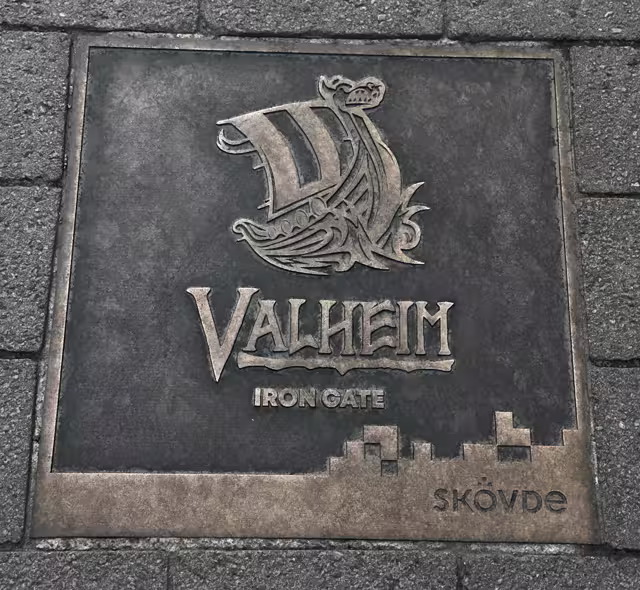 A bronze pavement plaque showing the Valheim longship logo, the words Valheim and Iron Gate, and the Skövde city mark.