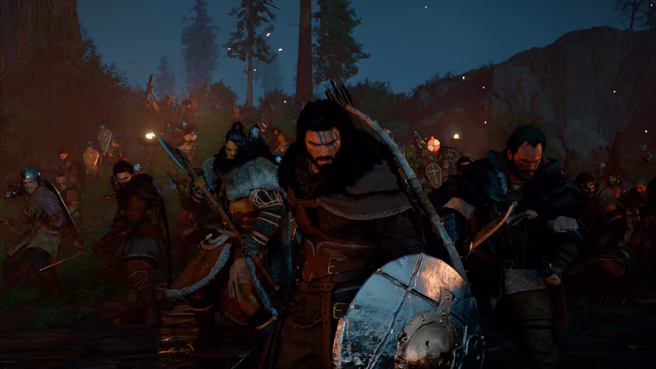At night in a pine forest, a crowd of warriors runs toward the viewer. At the front a man with long dark hair and blue paint across his eyes carries a round metal shield and a bow, flanked by fighters in furs with axes and spears. Torches light the trees behind them.
