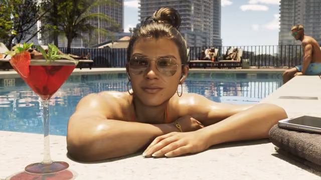 A woman in aviator sunglasses and hoop earrings leans her folded arms on the edge of a swimming pool, a red cocktail garnished with a strawberry and a phone on a towel beside her, with sunbathers, palm trees and tall towers behind.