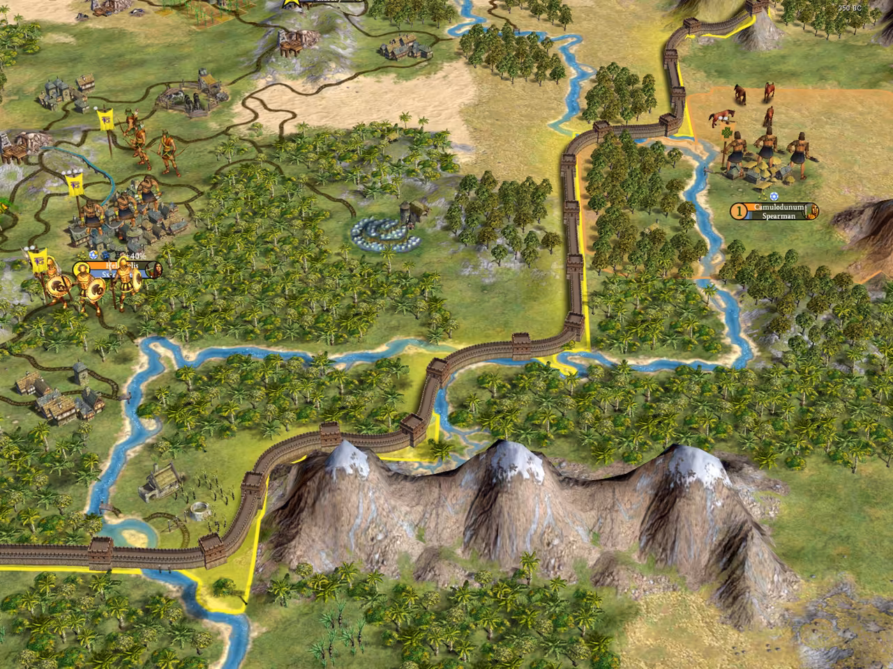 3D map of forest, rivers and roads with a brown crenellated wall winding along a yellow border line over a range of snowy peaks; a label at right reads Camulodunum, Spearman, and soldiers with yellow banners stand at left.