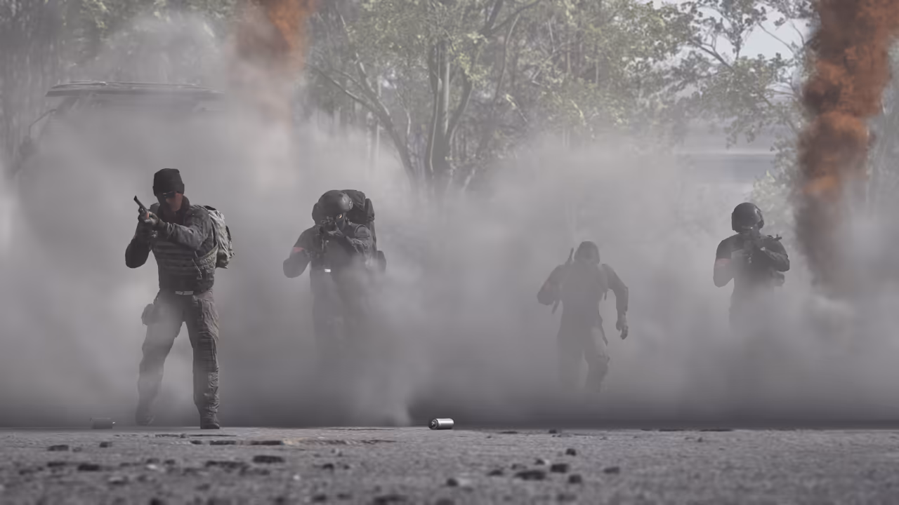 Four soldiers in helmets and vests emerge from a gray smoke cloud toward the camera on a paved road, trees and a dark plume of smoke behind them.
