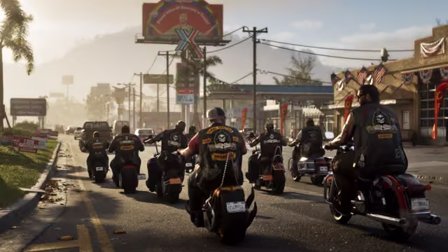 Seen from behind, a line of bikers in black vests with skull patches rides heavy motorcycles along a sunny road lined with political signs, American flags, a gas station and a large billboard, toward hills in the haze.