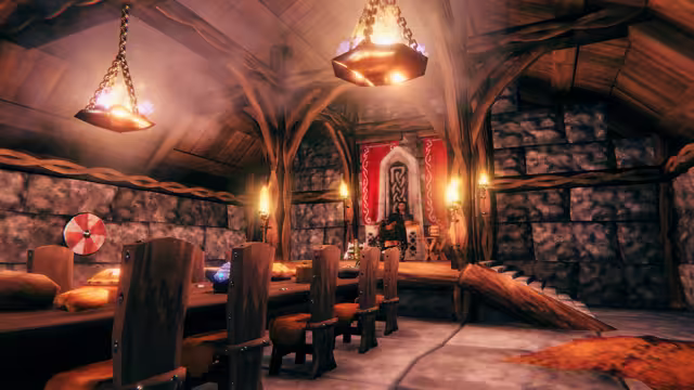 Screenshot of the inside of a stone longhouse lit by hanging iron braziers, with a long wooden table, carved chairs, banners and a raised timber roof