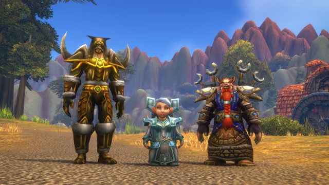 A bearded human in green and gold mail with a wolf-head helm and curved horn shoulder guards, a small gray-haired gnome woman in a teal robe with square shoulder pieces, and a red-bearded dwarf in blue and brown mail with horn-shaped shoulder ornaments stand side by side on a dusty road. Behind them are pine trees, a steep range of red-topped peaks and a house with a red tiled roof and a water wheel.