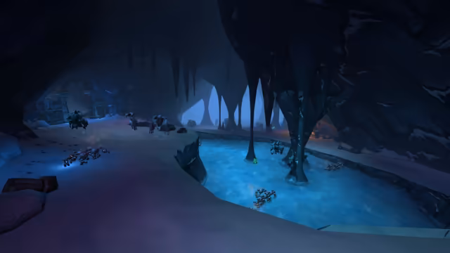 A wide, dim blue cave with a snow-covered floor curves around a sheet of glowing frozen water, where tall dark rock columns reach down from the ceiling. Clusters of rocky, many-limbed creatures move over the snow and the ice, a wooden crate sits in the foreground, and a ruined stone archway stands at the far left.