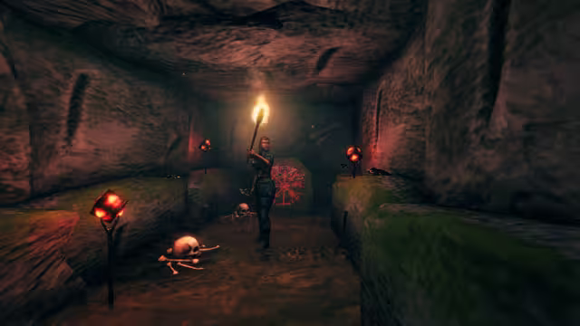A woman holding a torch stands in a narrow stone tunnel with mossy ledges; glowing red cubes sit on forked iron stands, skulls and bones lie on the floor and a red compass-like rune is painted on a stone behind her.