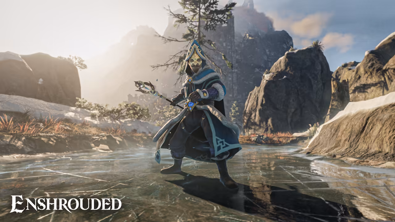 Bright winter sun over a frozen lake with cracked, reflective ice. In the center a figure in a long blue and white robe with a tall hood and a face covering holds a staff with a bright tip. Large rocks with snow on their tops surround the lake, a bare tree leans over at top, and mountains fade into the haze. The Enshrouded logo is at bottom left.