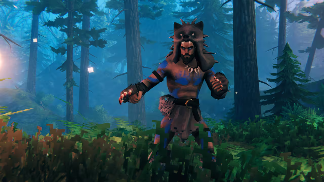 Screenshot of a bearded Viking in a bear-head hood, a necklace of teeth, blue body paint and a fur loincloth, clawed gauntlets raised, standing in a misty pine forest