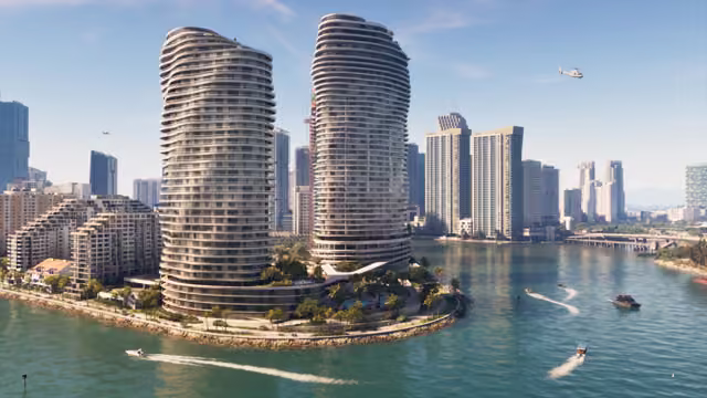 Two tall, wavy white skyscrapers rise from a landscaped point in blue-green water crossed by speedboats and jet skis, in front of more high-rise towers, a causeway and a helicopter in a clear sky.