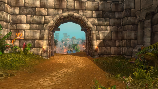 A wide dirt road framed by tropical flowers and ferns leads through an arched wooden gate set in a wall of huge gray stone blocks, with a torch burning on each side. Through the opening, red rock, palm trees, a blue-roofed structure and pale stone towers stand under a turquoise sky.