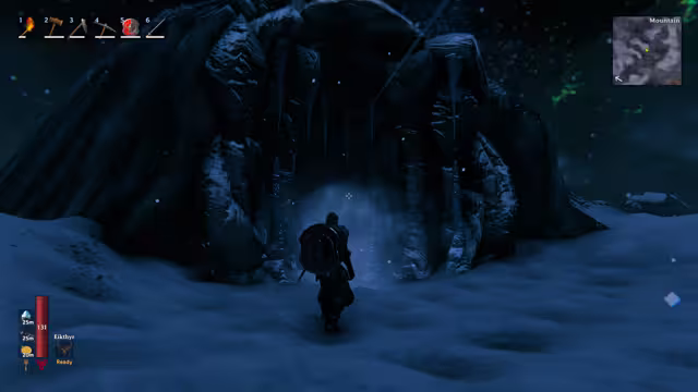 A Viking with a round shield on his back stands in deep snow before a dark rock cave mouth fringed with long icicles, a pale mist inside; the HUD minimap is labeled Mountain.